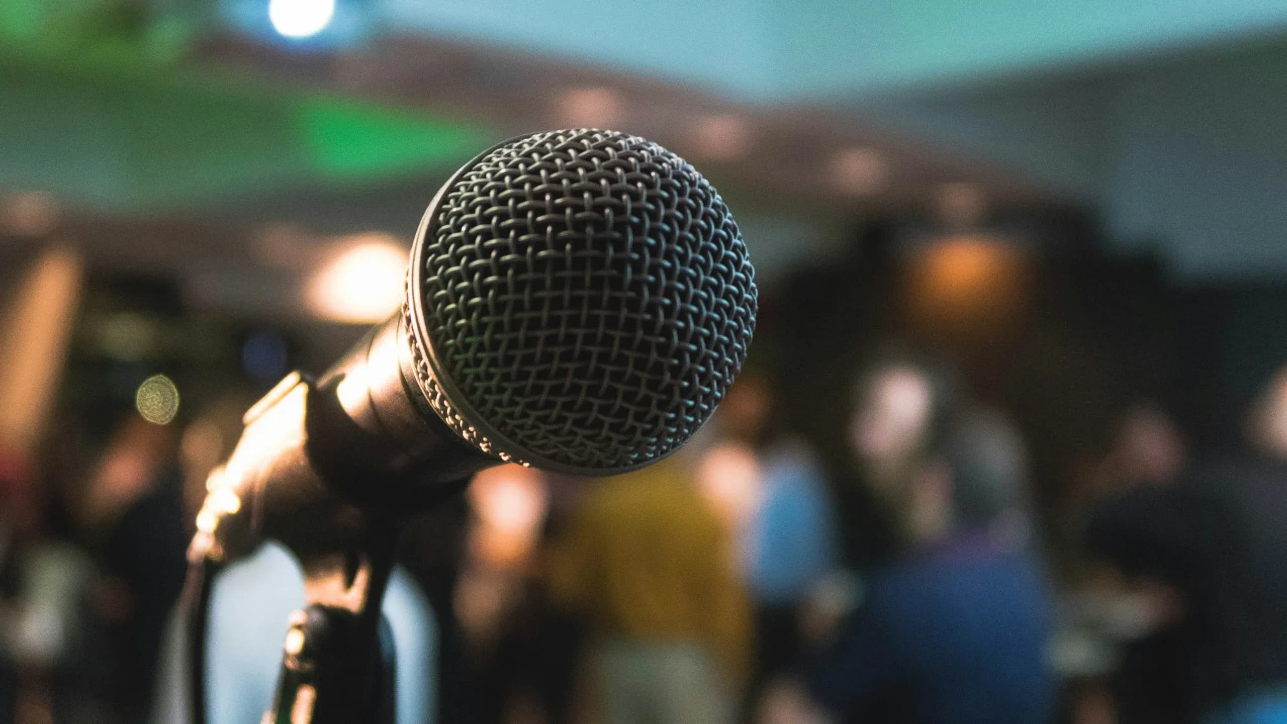 A stage microphone in close focus, an audience blurred behind it