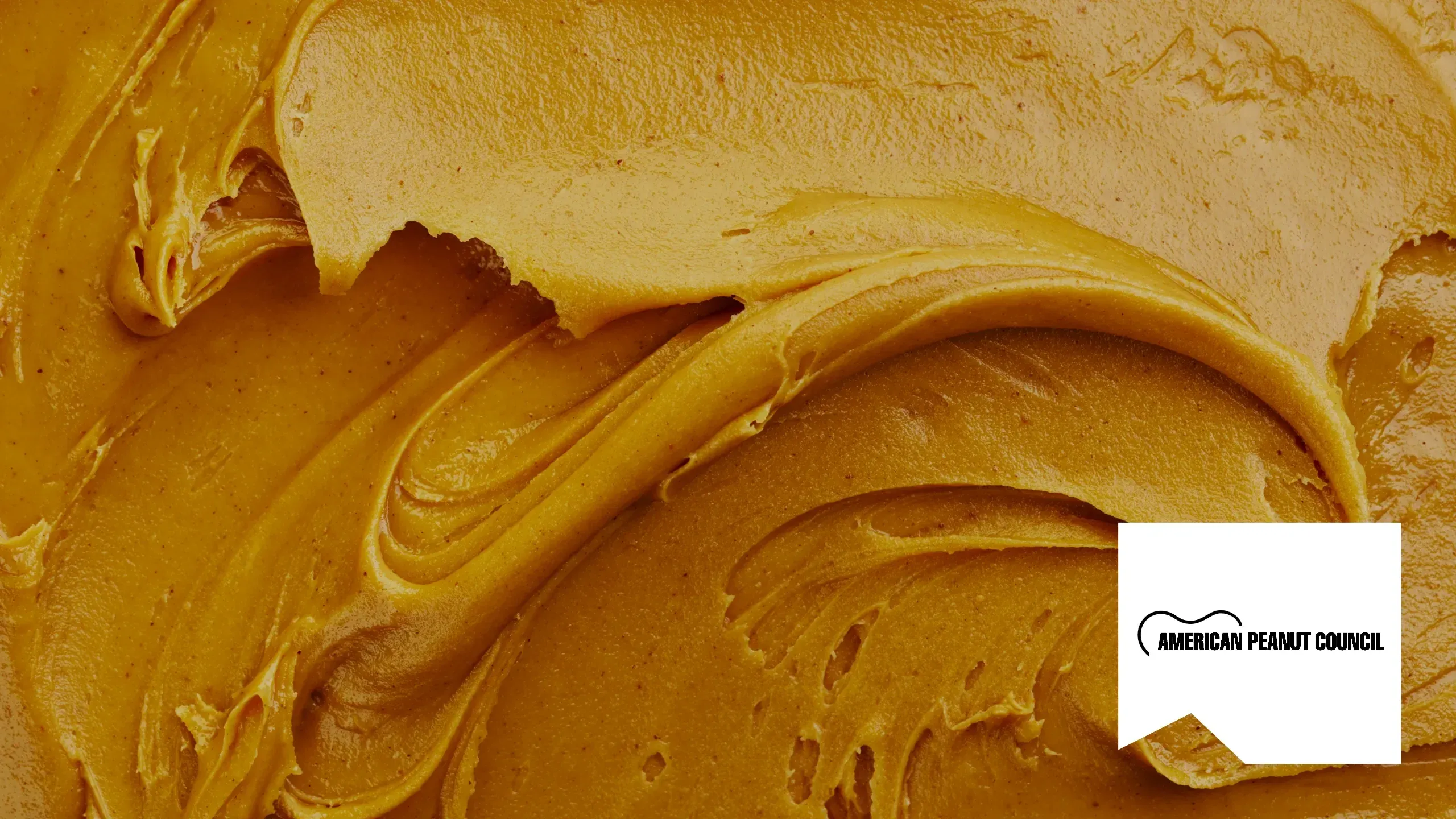 A close-up of swirled peanut butter, with the American Peanut Council logo on a white panel in the corner